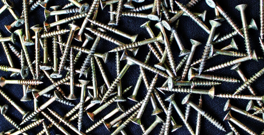 Pile of silver flat head screws on a dark background